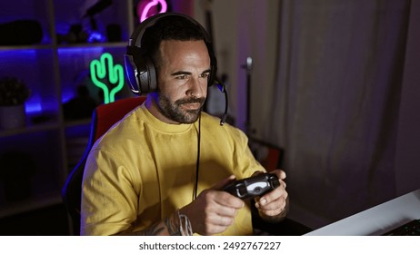 Focused hispanic man with beard playing video games in a dark room at night, wearing headphones. - Powered by Shutterstock