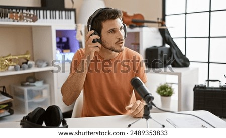 A focused hispanic man with a beard prepares for a podcast in a modern studio, adjusting his headphones.