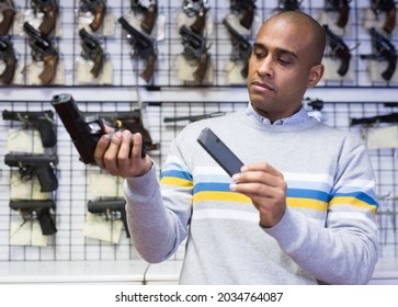 Focused Hispanic Man Examining Handgun Before Buying At Gun Shop, Inserting Magazine In Pistol Grip