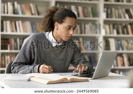 Focused Hispanic student guy sit at desk in library, studying using laptop, e-learns, improve subject knowledge, preparing to enter higher education institution using application. Gen Z and education