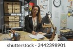 Focused hispanic woman detective working late in a cluttered police station office.