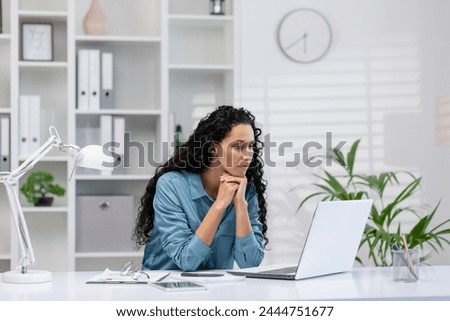 Focused Hispanic woman working on her laptop from a well-organized home office, exuding professionalism and concentration.