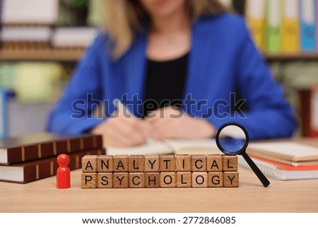 A focused individual writes notes while examining the concept of analytical psychology. Books and a magnifying glass are arranged neatly, emphasizing the pursuit of knowledge and insight