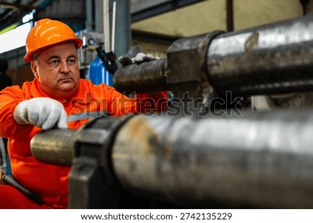 Focused industrial engineer with diligent expression working heavy machinery maintenance using large metal cylinder component factory workshop manufacturing plant with professional safety gear