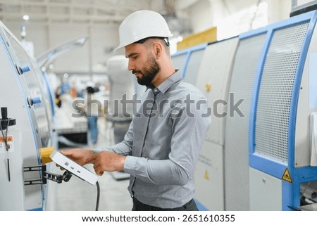 Focused industrial engineer using digital tablet, managing machinery on automated production line in modern factory, optimizing manufacturing process
