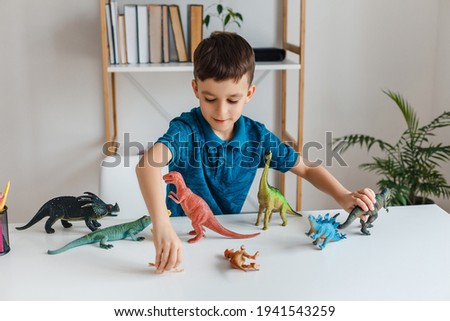 Focused kid playing with dinosaurs at home. Boy learning paleontology by dino toys at leisure. Concept of clever child and early education