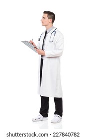 Focused male doctor in white lab coat holding a clipboard and writing. Full length studio shot isolated on white.