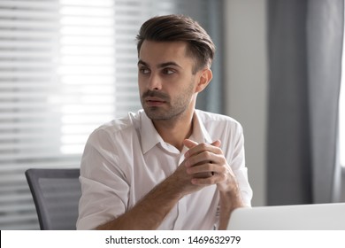 Focused Male Employee Sit At Workplace Look To Side Listen To Someone Talking In Office, Thoughtful Pensive Man Worker Distracted From Work Interested In Coworker Or Colleague Conversation