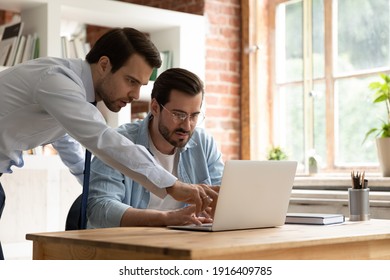 Focused male employees brainstorm cooperate on computer in office, discuss company business project together. Concentrated men coworkers work on laptop analyze corporate research or report online.