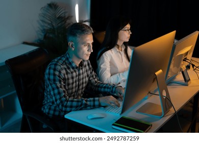 Focused Male And Female Professionals Working Late At Night On Desktop Computers In A Modern Office Environment - Powered by Shutterstock