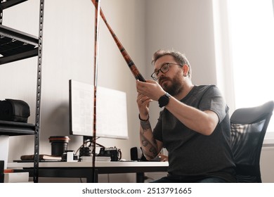 A focused male photographer reviews film negatives against natural light in his well-lit, modern office workspace surrounded by photography equipment. - Powered by Shutterstock