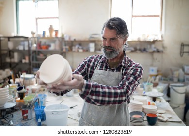 Focused male potter examining his creation for flaws in the pottery workshop - Powered by Shutterstock