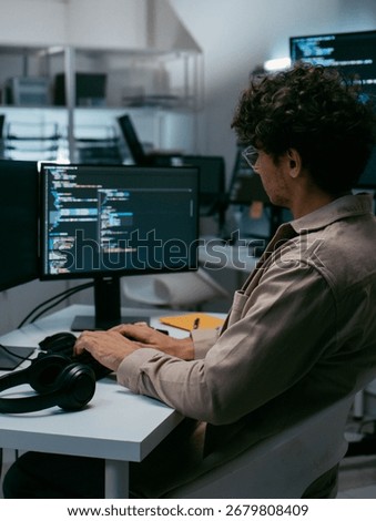 Focused Male IT Programmer working in software developing office, Writing code using desktop computer review and analysis data on monitor screen developing a new software app development project.
