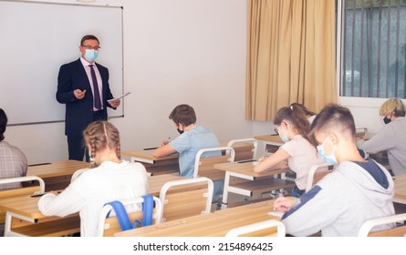 Focused Male Teacher In Protective Face Mask Giving Lesson To Teenage Students In College. New Life Reality During Coronavirus Pandemic