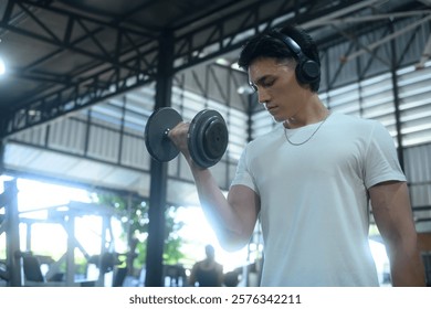 Focused man doing weight training at the gym while listening to music on headphones
