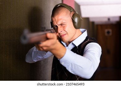 Focused Man In Ear Protectors Aiming Single Barrelled Shotgun At Target In Shooting Range.