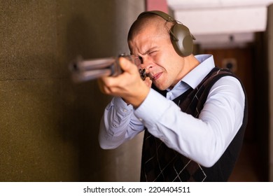 Focused Man In Ear Protectors Aiming Single Barrelled Shotgun At Target In Shooting Range.