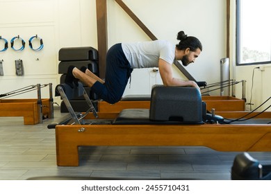 Focused man engaged in a workout using a pilates reformer apparatus in a fitness studio - Powered by Shutterstock