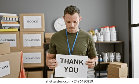 A focused man holds a 'thank you' sign at a donation center, flanked by boxes and supplies.