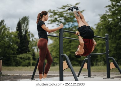 Focused man inverting on outdoor fitness equipment while his partner assists, demonstrating teamwork and physical strength in a tranquil park setting. - Powered by Shutterstock