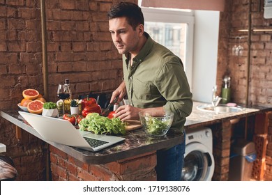 Focused man with a knife in his hand staring at his laptop on the countertop - Powered by Shutterstock