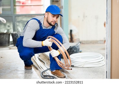 Focused Man Running Cable And Conduit Through Concrete Trench At Indoor Construction Site