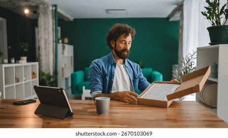 Focused man sitting at a dining table, eagerly opening a package containing a paint by numbers kit, ready to dive into a new creative hobby and express artistic flair