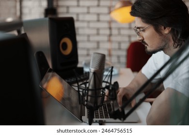 Focused man working on a laptop in a home recording studio with a microphone setup, surrounded by audio equipment. - Powered by Shutterstock