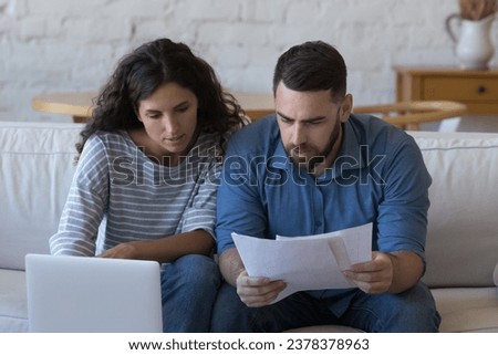 Focused married couple reading paper documents at laptop, reviewing real estate property buying contract, mortgage, insurance agreement, bank notice, doing household paperwork together