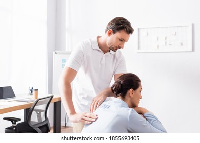 Focused Masseur Looking At Brunette Woman, While Doing Back Massage In Office