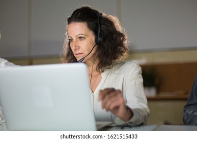 Focused Mature Call Center Operator Looking At Laptop. Serious Curly Woman Working In Office. Call Center Concept