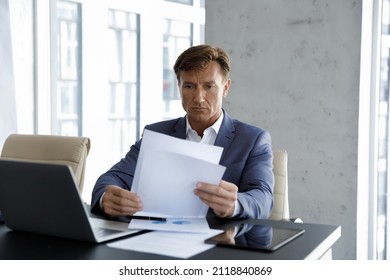Focused Mature Company Executive Reviewing Sales Reports, Checking Documents At Laptop On Workplace, Reading Corporate Papers, Analyzing Marketing Data, Statistic Research. Business, Paperwork Concept