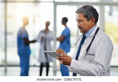 Focused And Mature Doctor Browsing On A Digital Tablet While Working In The Hospital. Using Wireless Technology To Diagnose Diseases In The Health Medicine Field. Researching Medical Resources