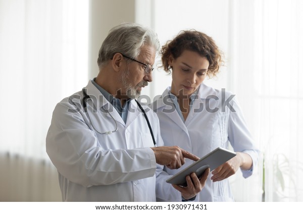 Focused\
mature male doctor and female nurse look at tablet screen discuss\
anamnesis together. Concentrated diverse medical professionals use\
pad device, engaged in team thinking in\
hospital.