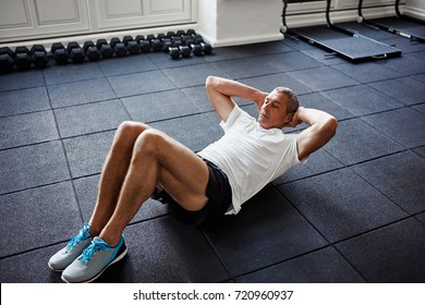 Focused mature man in sportswear lying on the floor doing sit ups alone while working out in a gym - Powered by Shutterstock