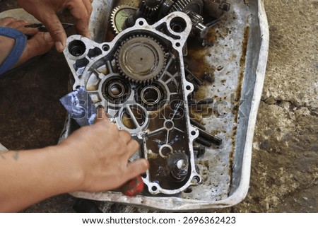 Focused mechanic hand performing engine repair and maintenance service in workshop. Close up detail of machine part with gear and cog assembly getting cleaned