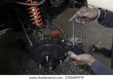 Focused mechanic hand using tool for vehicle brake system repair and service. In garage, this work involves careful adjustment of orange suspension component