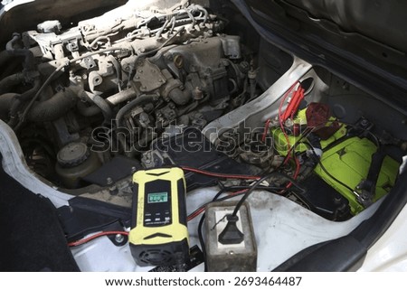 Focused mechanic performs car engine maintenance and repair. vehicle battery charger or jump starter gets connected to solve power problem. Automotive work in garage