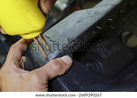 Focused mechanic using yellow plastic welder tool for car bumper crack repair. worker melts and joins broken part with precision in workshop service garage for maintenance