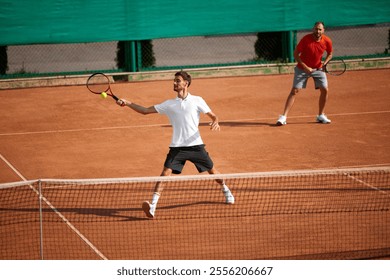 Focused men, friends playing tennis on outdoor clay court, growing skills, attention and teamwork cooperation during game. Concept of sport, competition, active and healthy lifestyle - Powered by Shutterstock