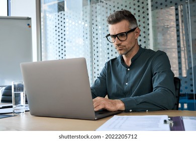 Focused Middle Aged Business Man Typing On Computer Working In Modern Office. Serious Busy Male Manager Executive Using Software Laptop Analyzing Digital Tech Data Doing Market Research At Workplace.