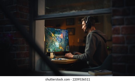 Focused Middle Aged Male Gamer Playing Online Video Game On Personal Computer. Guy Enjoying Fantasy RPG Game With Role Playing Character Casting Spells, Destroy Enemies. Shot From Outdoors.