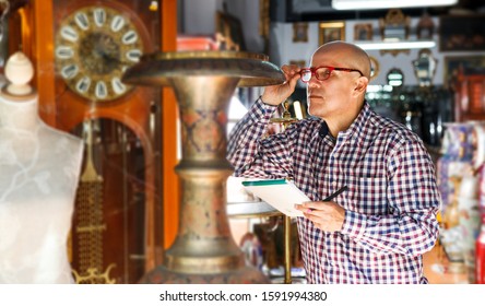 Focused Middle Aged Man Owner Of Antiques Shop Inventorying Vintage Goods