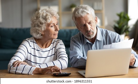 Focused middle aged retired family couple managing monthly budget, involved in financial paperwork, paying taxes online using e-banking computer application or calculating expenses together at home. - Shutterstock ID 1896311551