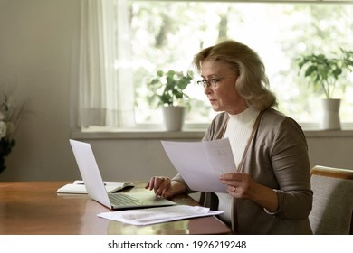 Focused Middle Aged Woman Holding Document And Using Laptop At Home. Female Adult Pensioner Checking Life Insurance Or Savings Financial Account, Paying Bill On Bank Online App, Planning Budget