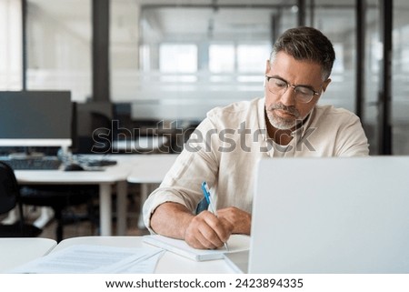 Focused middle-age Hispanic man using laptop computer for business studying, watch online virtual webinar training meeting, video call, make notes. Mature Latin businessman work in office, copy space.