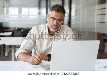 Focused middle-age Hispanic man using laptop computer for business studying, watch online virtual webinar training meeting, video call, make notes. Mature Latin businessman work in office, copy space.