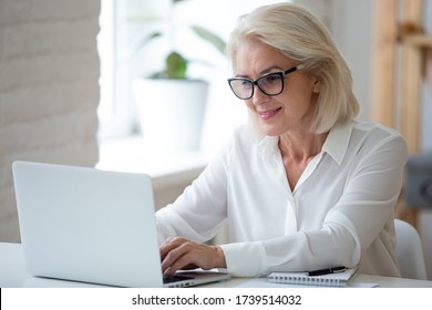 Focused Middle-aged Businesswoman In Glasses Sit At Desk Typing Working On Laptop, Browse Wireless Internet, Concentrated Senior Female Employee Consult Client Online Using Modern Computer Gadget