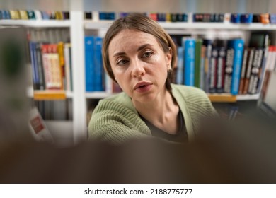 Focused Middle-aged Woman In Bookstore Choosing Book While Walking Alongside Rows Of Bookshelves. Closeup Of Female Student Doing Research In Library, Getting Second Degree. Education Has No Age