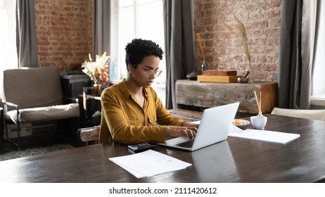 Focused millennial African owner woman using payment banking financial online app on laptop computer, working on domestic paper documents, paying bills, calculating taxes, insurance, mortgage fees - Shutterstock ID 2111420612
